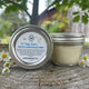 Garden Path Homemade Soap's Wiggle Baby Butter on wooden stump with tiny white flowers .