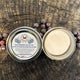 Open tin of body butter with a label on a wooden surface with black raspberries.