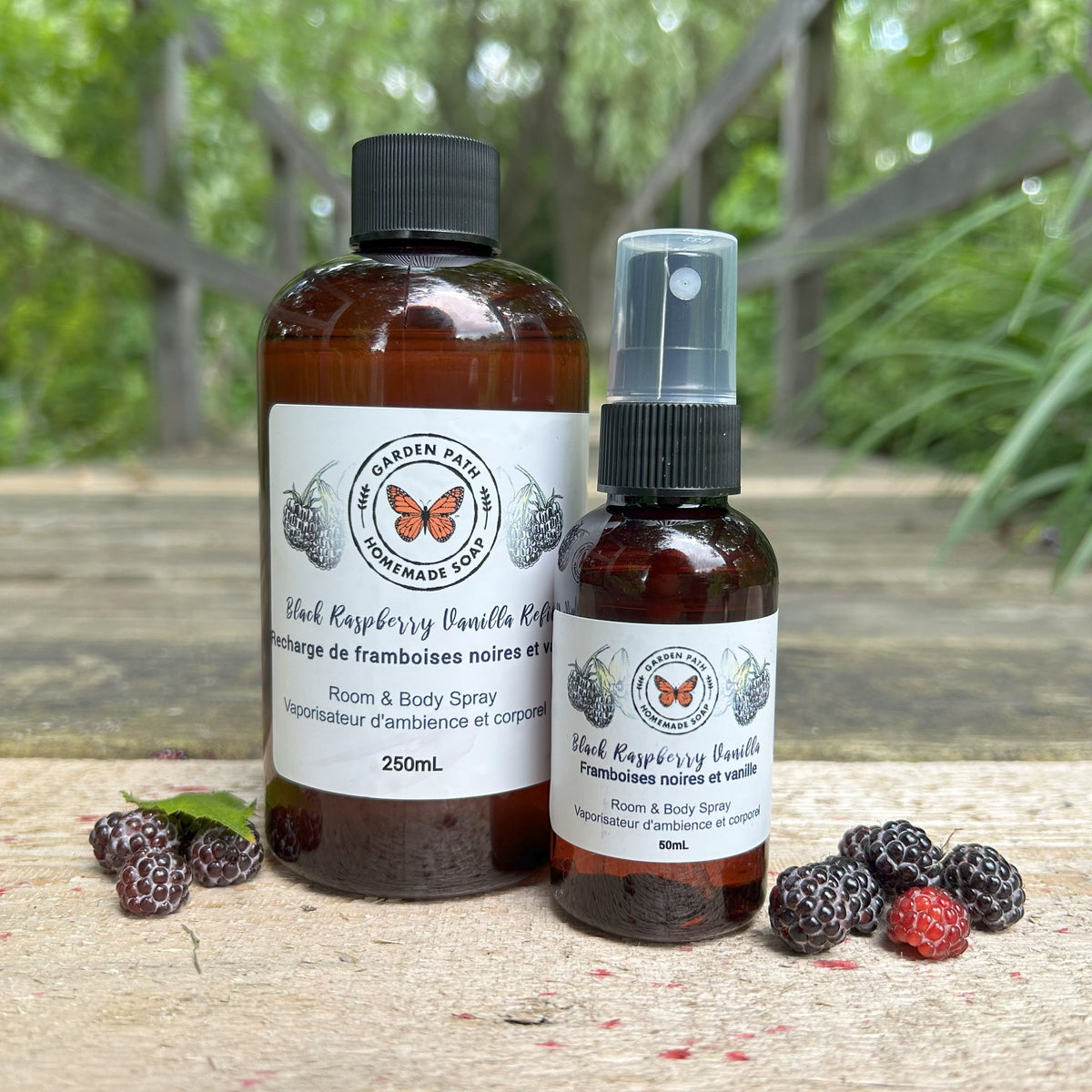 Black Raspberry Vanilla Body & Room Sprayer and refill bottle by Garden Path Homemade Soap on a wooden surface with black raspberries.
