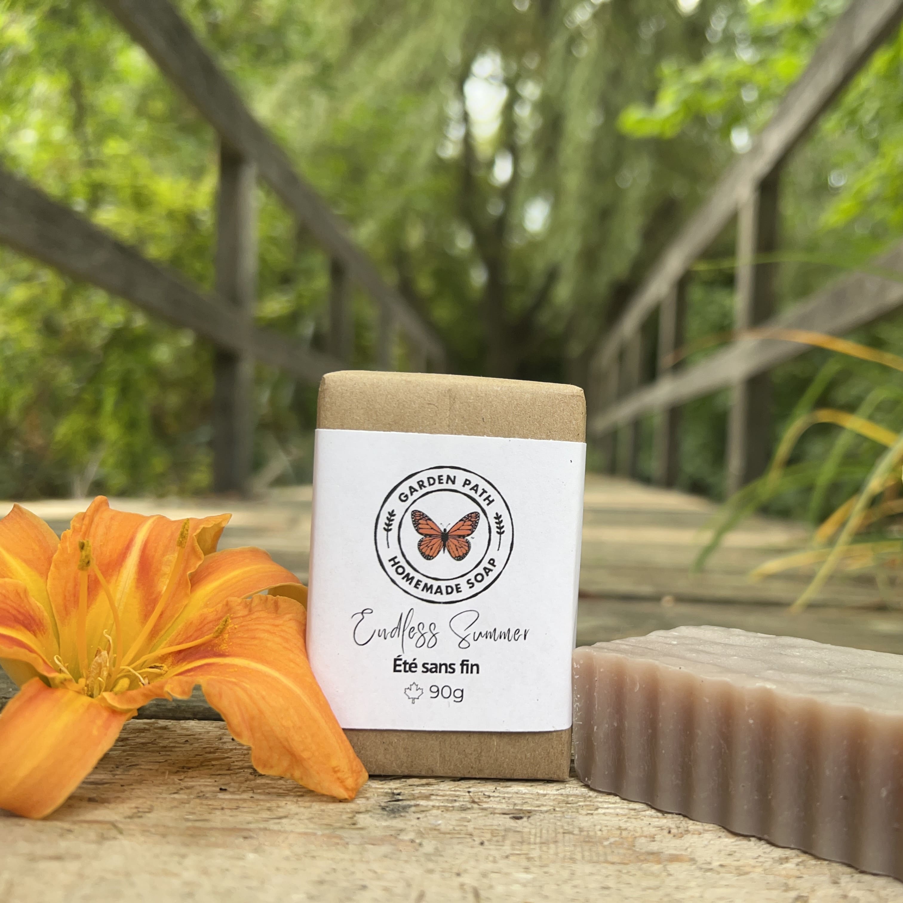 Endless Summer Bar of soap with a label featuring a butterfly and text, placed on a wooden surface with an orange flower and blurred green background.