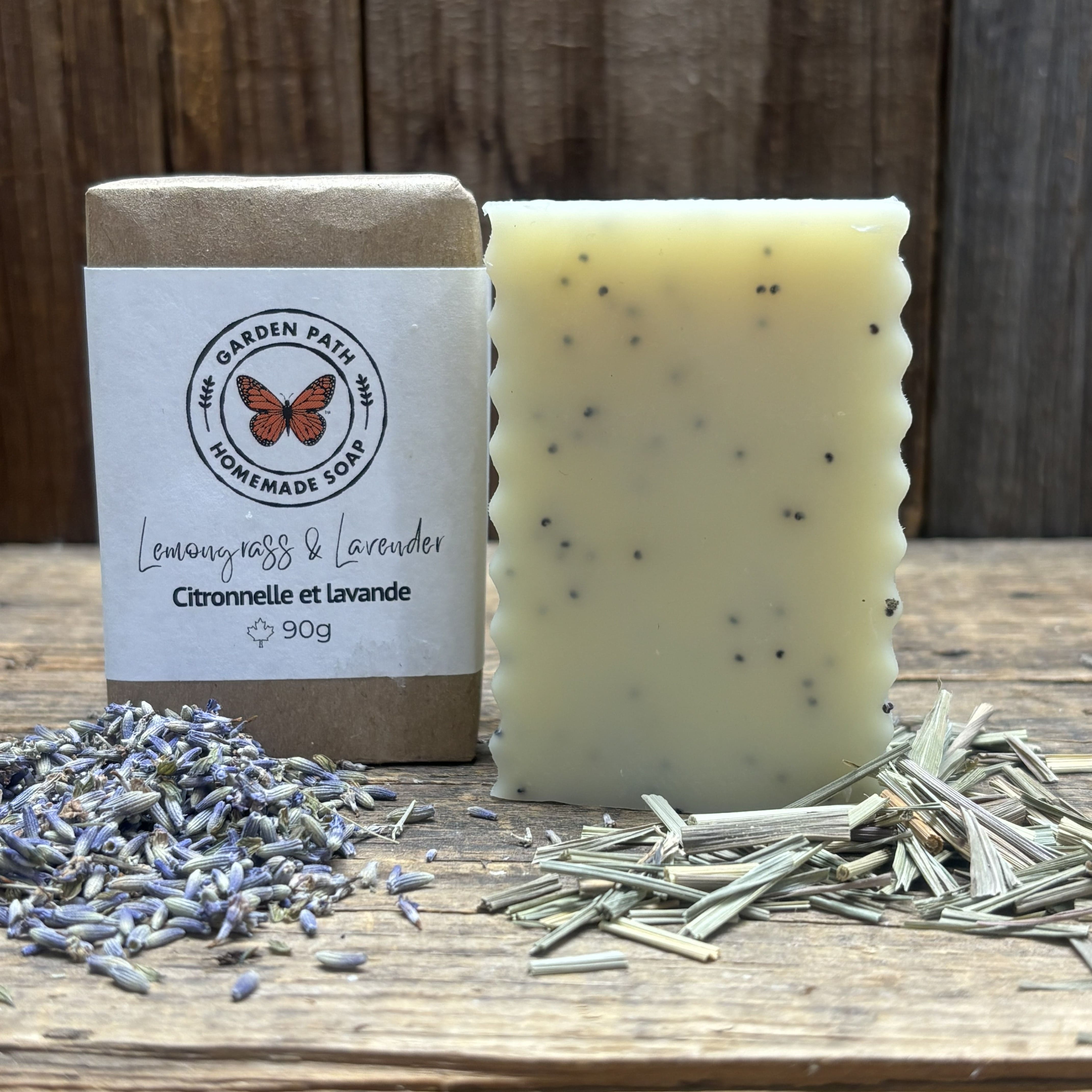 Lemongrass & Lavender Bar of soap with packaging labeled 'Garden Path Homemade Soap' on a wooden surface with lavender and lemon grass. 100% Natural Exfoliating Soap with Essential Oils