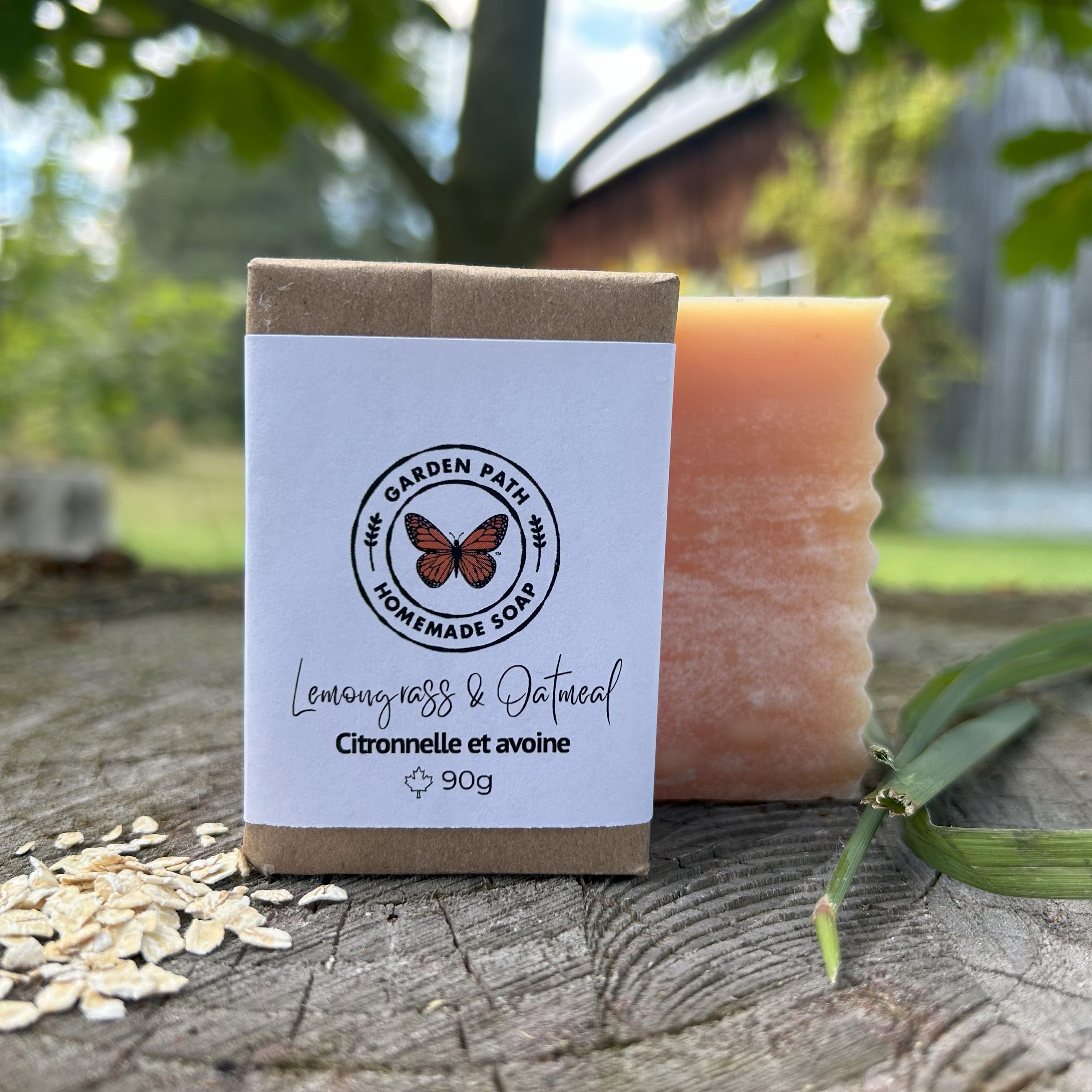 Lemongrass & oatmeal bar of soap with packaging labeled 'The Garden Path Homemade Soap' on a wooden surface outdoors. 100% Natural Exfoliating Soap with Essential Oil