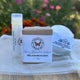 Lip balm, soap bar, and bath bomb from Garden Path Homemade Soap on a white organza fabric with a blurred floral background by Garden Path Homemade Soap.