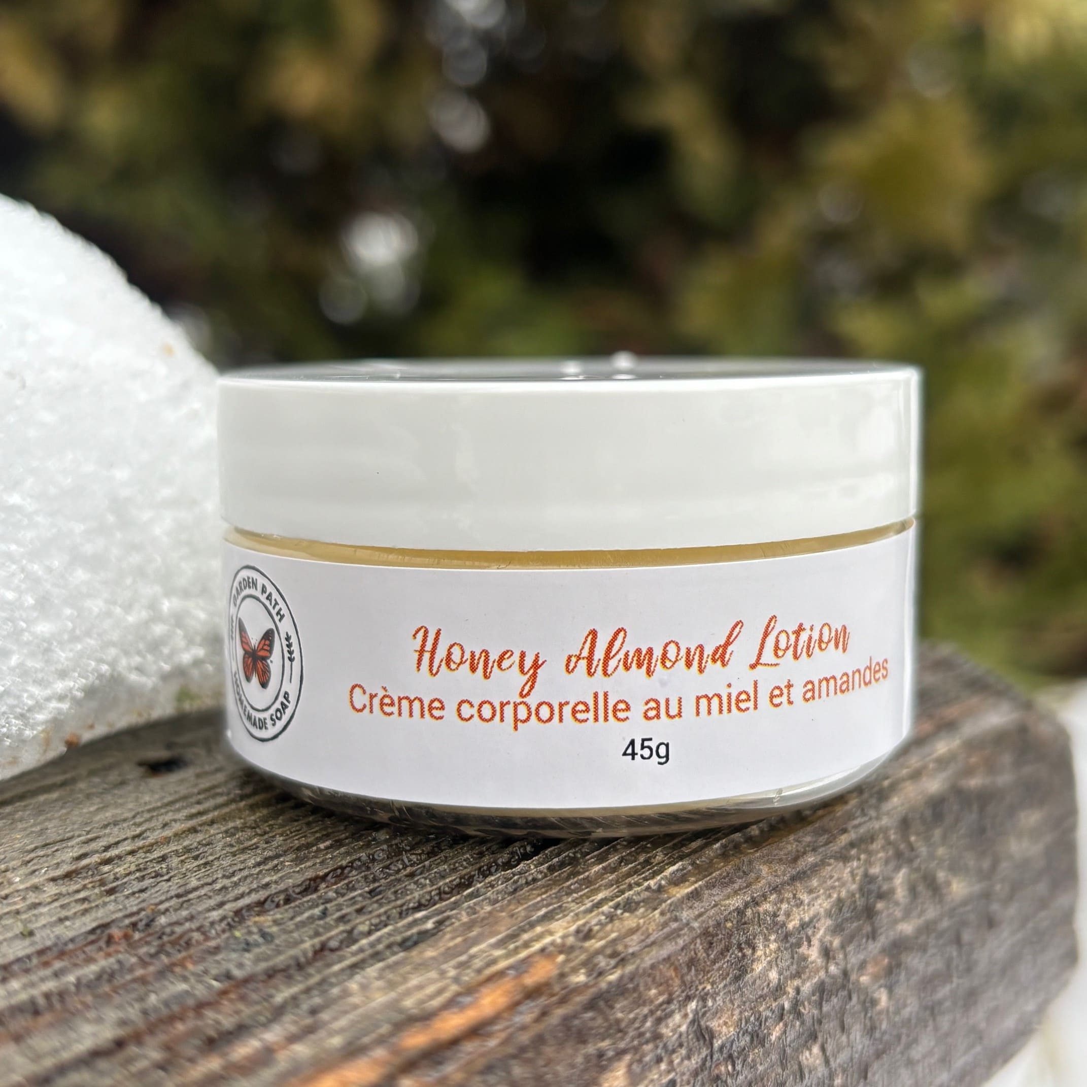 Jar of Garden Path Homemade Soap's Honey Almond Lotion on a wooden surface with a blurred natural background by Garden Path Homemade Soap