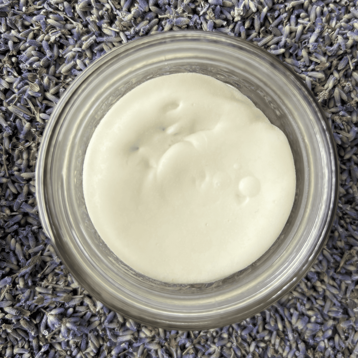 Open jar looking down from the top at creamy, white body butter surrounded by dried lavender buds.