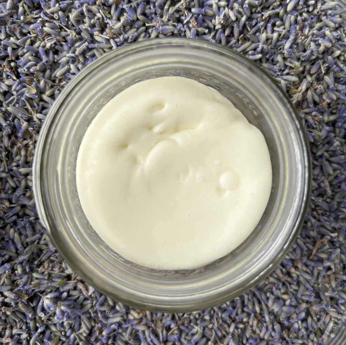 Open jar looking down from the top at creamy, white body butter surrounded by dried lavender buds.