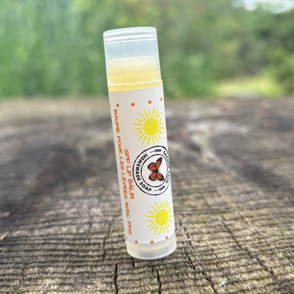 A stick of SPF lip balm placed on a wooden surface with a natural background by Garden Path Homemade Soap. 100% Natural Ingredients