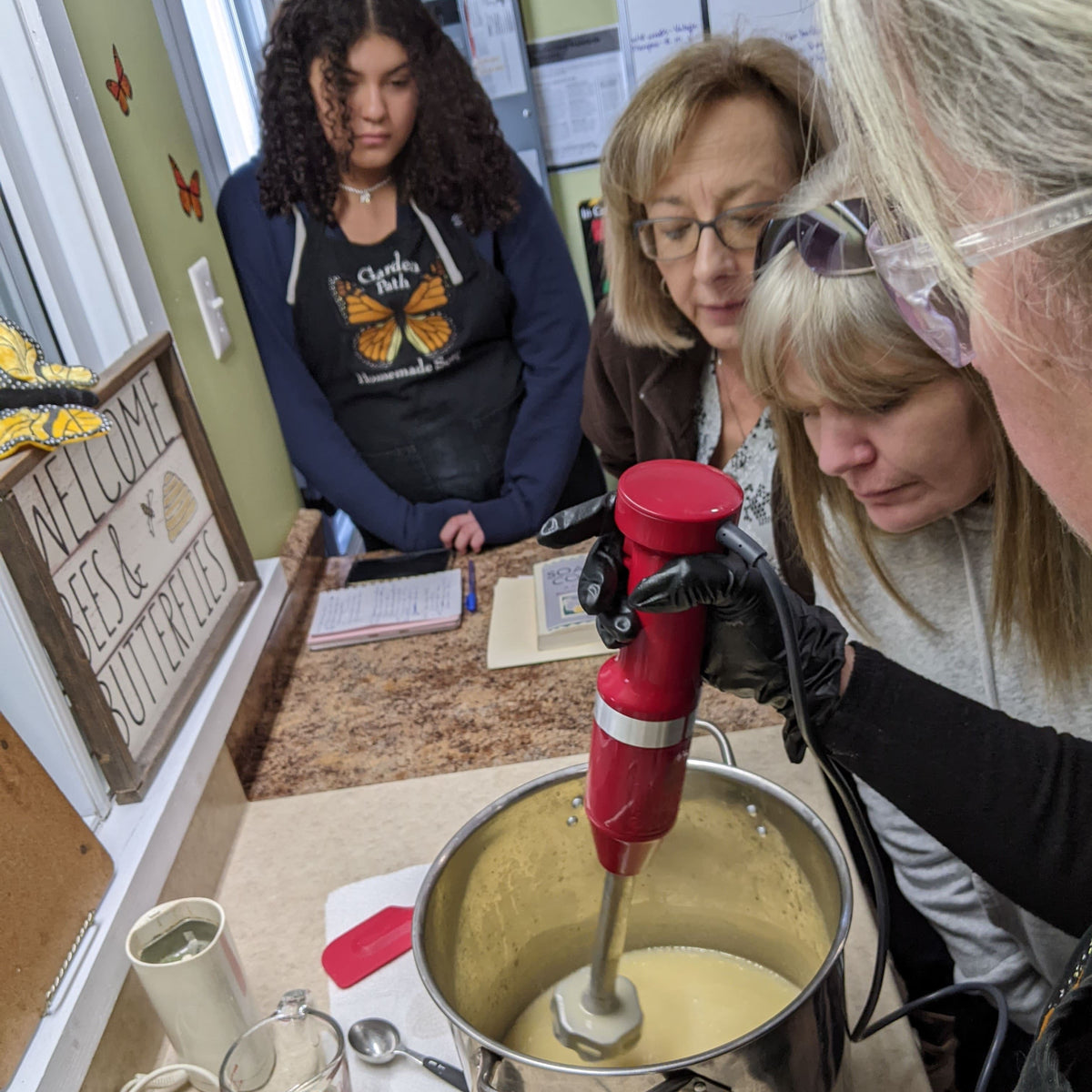 Three women watching the process of mixing soap