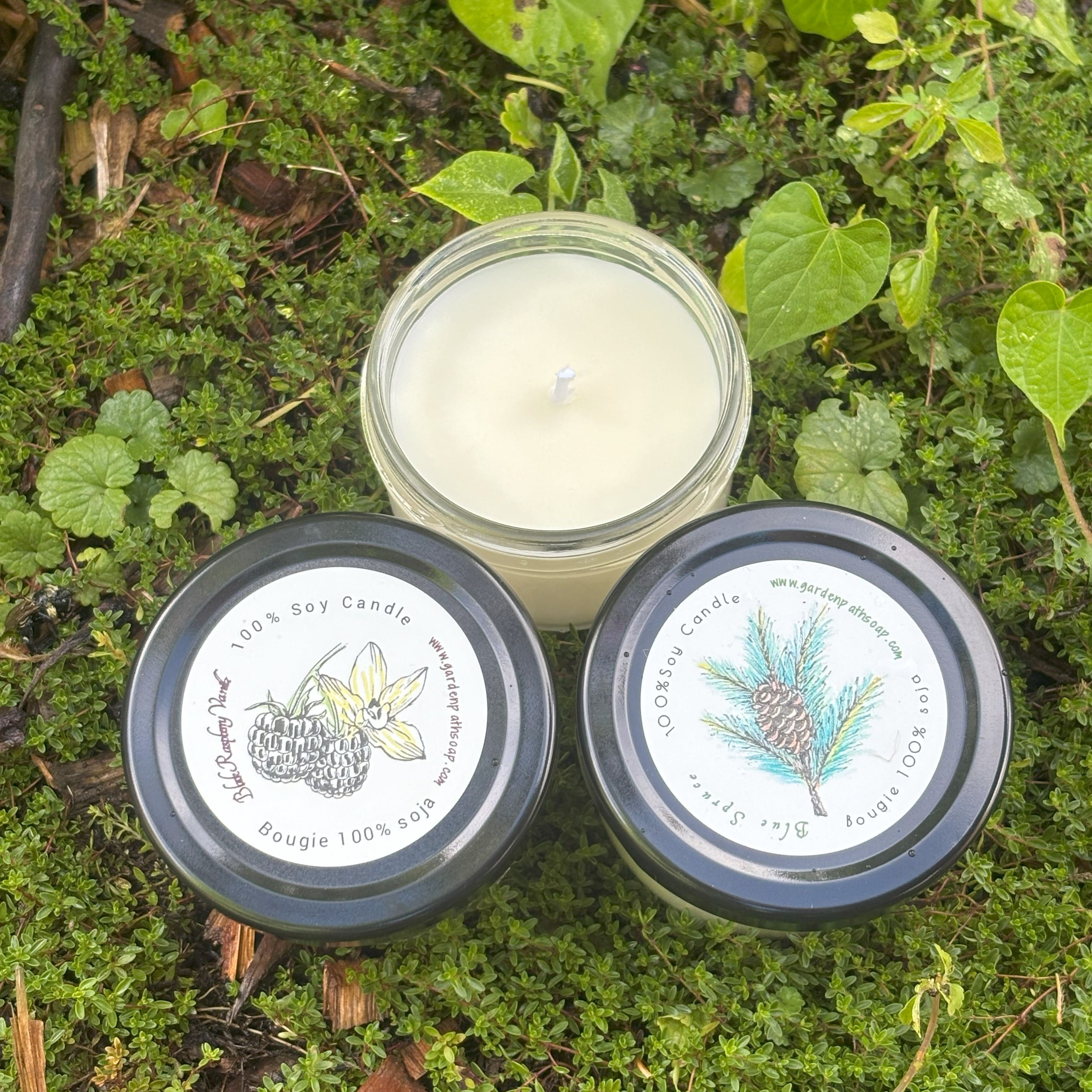 Two candles with labels on a green leafy background. One candle open to see the wick
