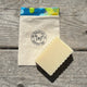 A handmade soap travel bag with a snap closure, featuring a colorful trim and the 'Garden Path Homemade Soap' logo on the front. A bar of soap is placed in front of the bag.
