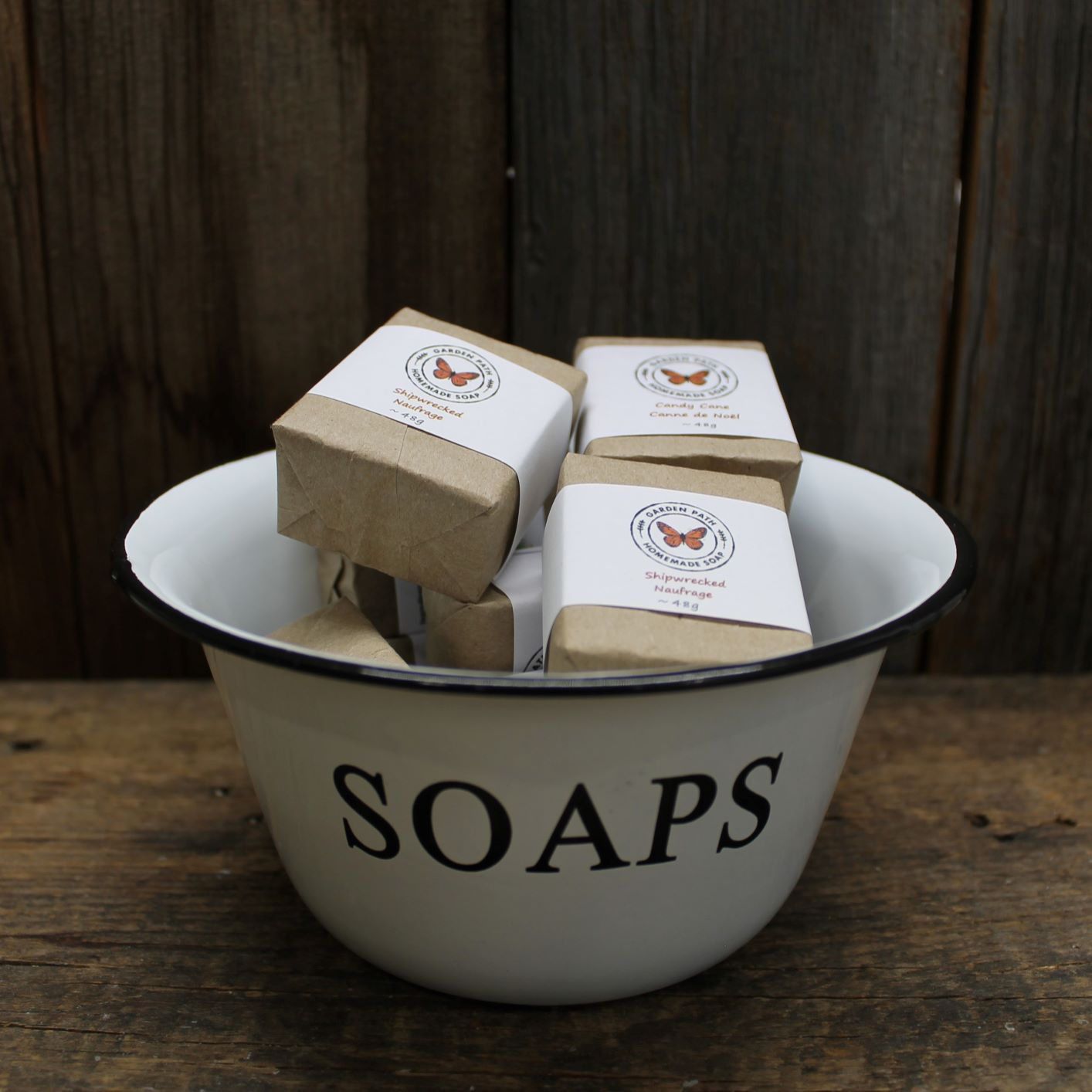 A bowl with the word 'SOAPS' on it, filled with small (mini), wrapped bars of garden path homemade soaps.