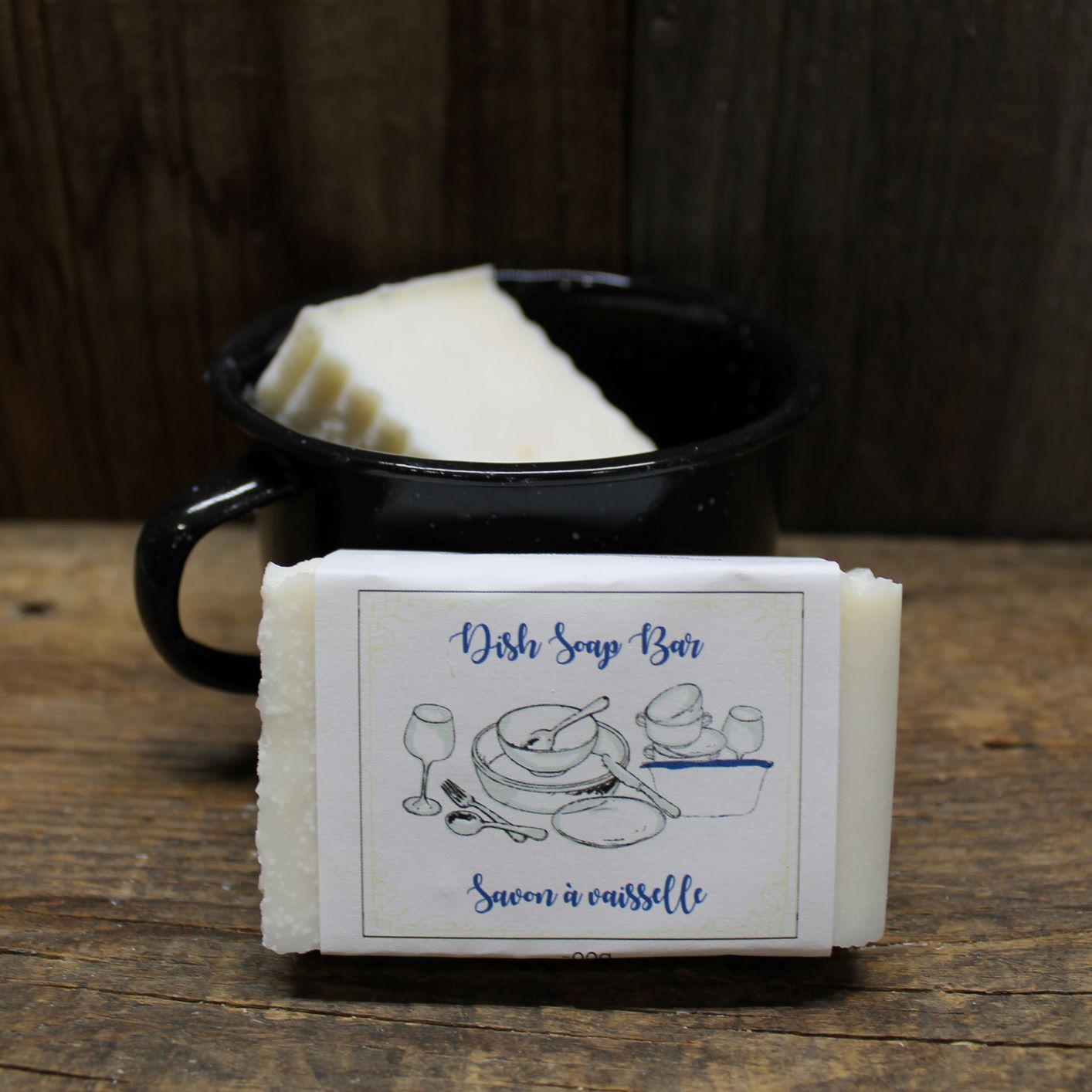 Dish Soap Bar sitting in front of a black mug that is also holding an unwrapped dish soap bar