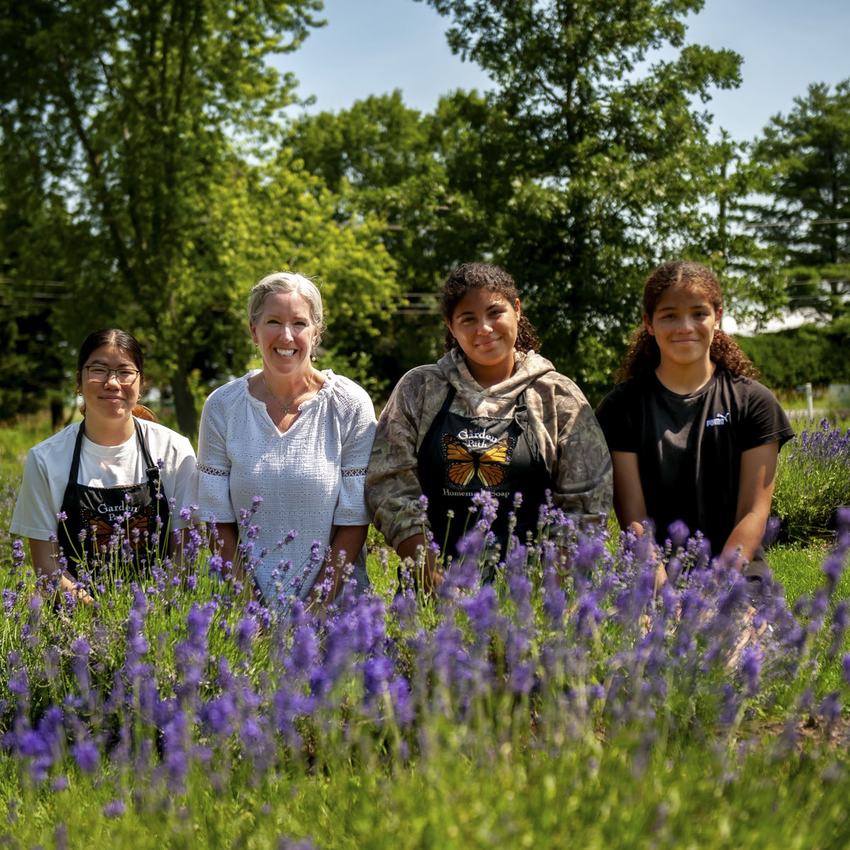 Four girls kneeling behind purple lavender with trees in the background