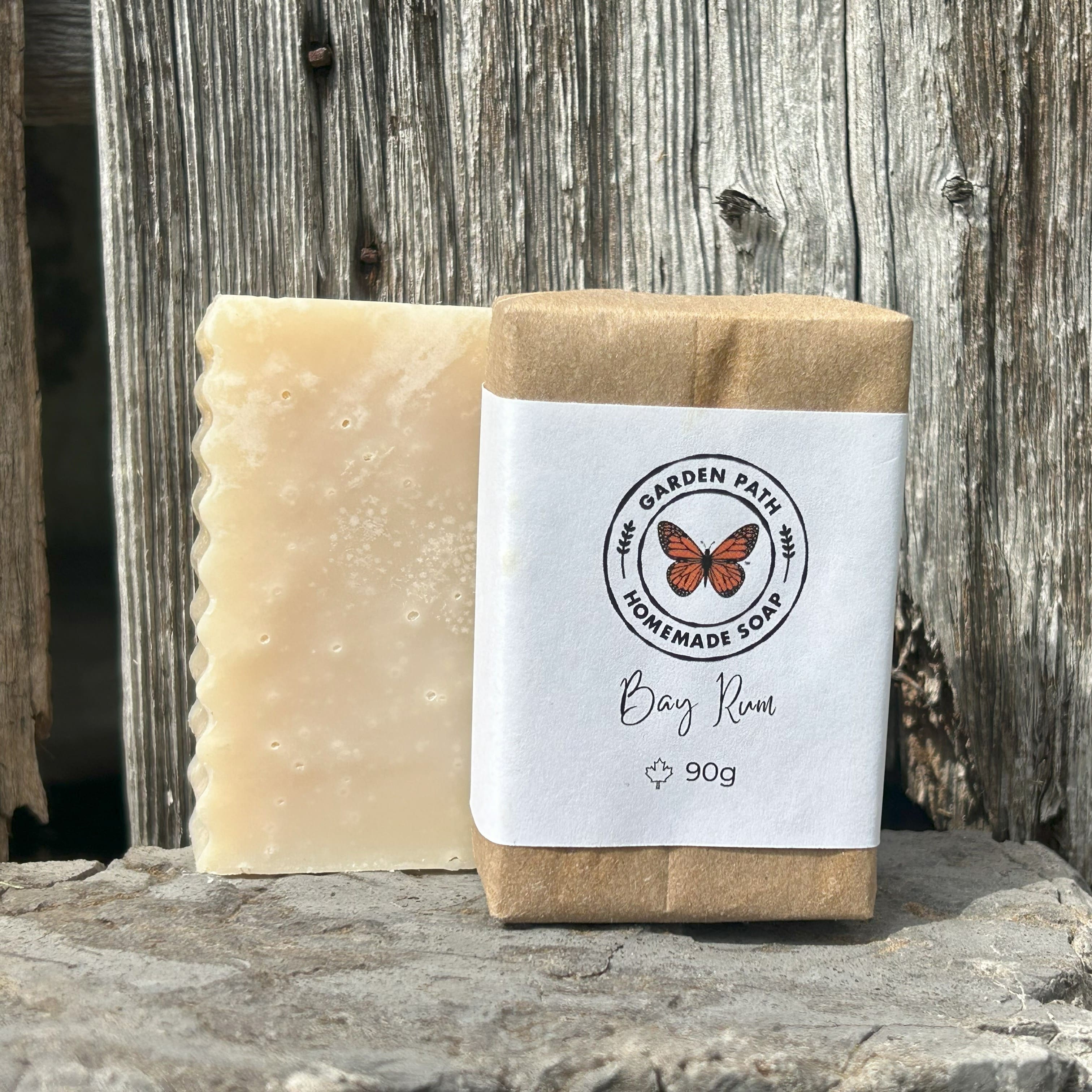 Bay Rum bar of soap both wrapped and unwrapped on a stone surface with a wooden barn board background by Garden Path Homemade Soap. Lightly Scented with Bay Rum Fragrance Oil