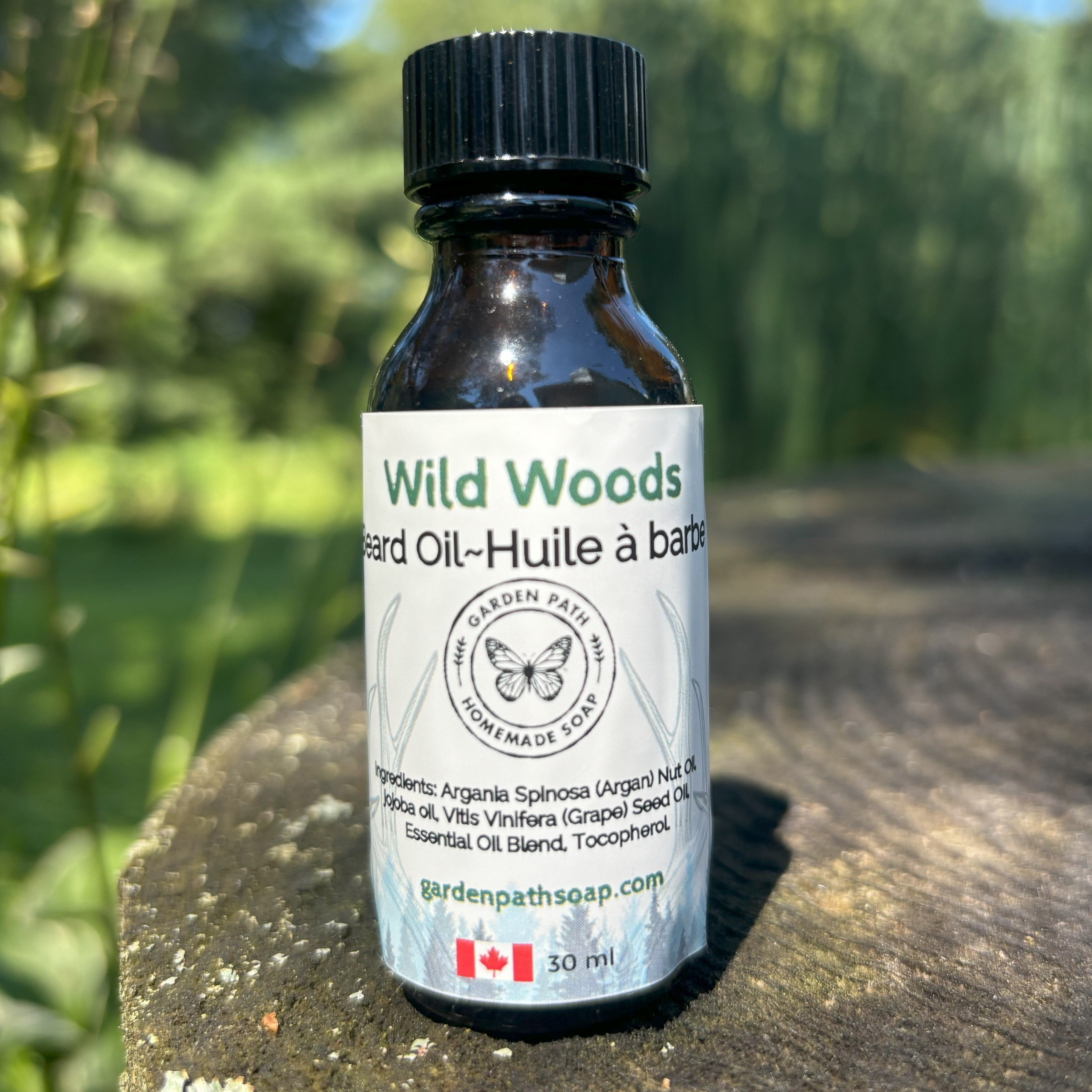 Wild Woods Beard Oil by Garden Path Homemade Soap sitting on a wooden surface with greenery in the background.