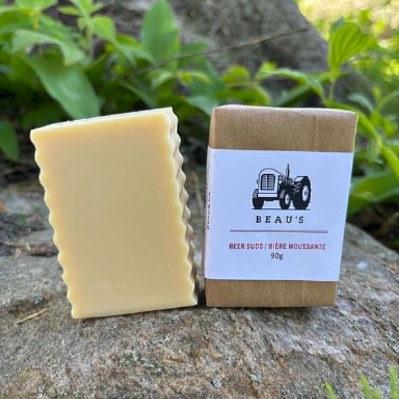Beau's Beer Suds Bar of soap both wrapped and unwrapped on a natural background with greenery around by Garden Path Homemade Soap. 100% Natural. Made with Beau's beer.
