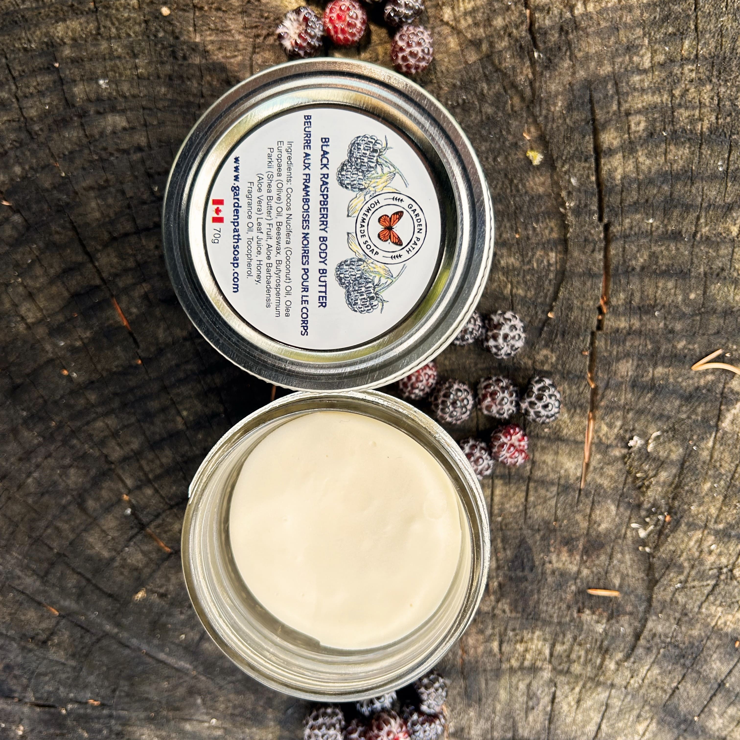 Open tin of body butter with a label on a wooden surface with black raspberries.
