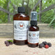 Black Raspberry Vanilla  Body & Room Sprayer and refill bottle by Garden Path Homemade Soap on a wooden surface with black raspberries.