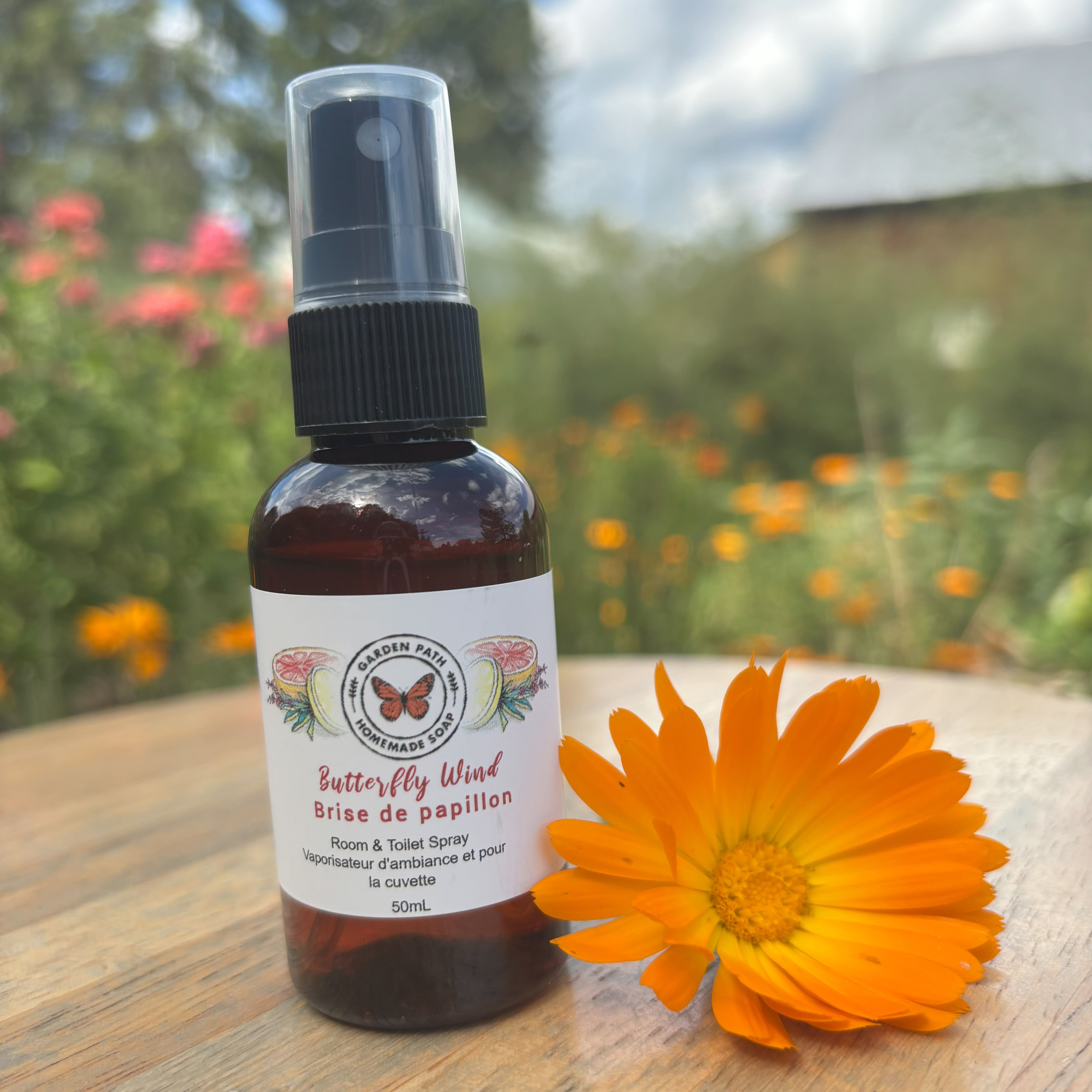 50 mL Butterfly Wind  Room & Toilet Spray bottle by Garden Path Homemade Soap on a wooder surface with  calendula flower. 100% Natural Essential Oil Blend