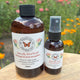 Butterfly Wind 50ml spray and 250ml refill bottle - Room & Toilet Spray by Garden Path Homemade Soap on a wooden surface with flowers in the background. 100% Natural Essential Oil Blend