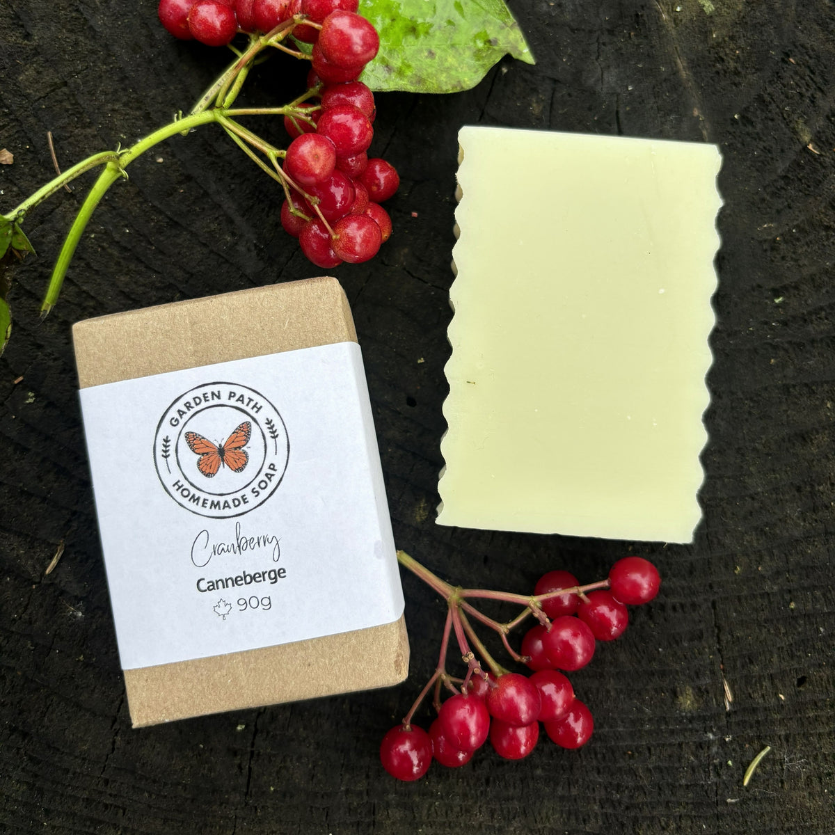 A handmade bar of soap in a pale yellow color, shown next to a wrapped bar of soap and red berries. Garden Path Homemade Soap 