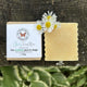 A handmade facial bar soap Clarify Facial Bar for acne care shown next to its paper packaging, placed on a rustic dark wood surface with white  flowers on top.  100% Natural Ingredients - Garden Path Homemade Soap