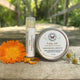 Healing Salve tube and tin on a wooden surface with flowers by Garden Path Homemade Soap. 100% Natural Ingredients & Essential Oils 
