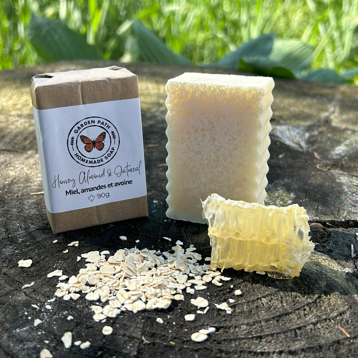 Honey Almond & Oatmeal Bar Soap on a wooden surface with oatmeal flakes and honeycomb beside the wrapped bar of soap  | Gentle Exfoliating Bar Soap - Garden Path Homemade Soap
