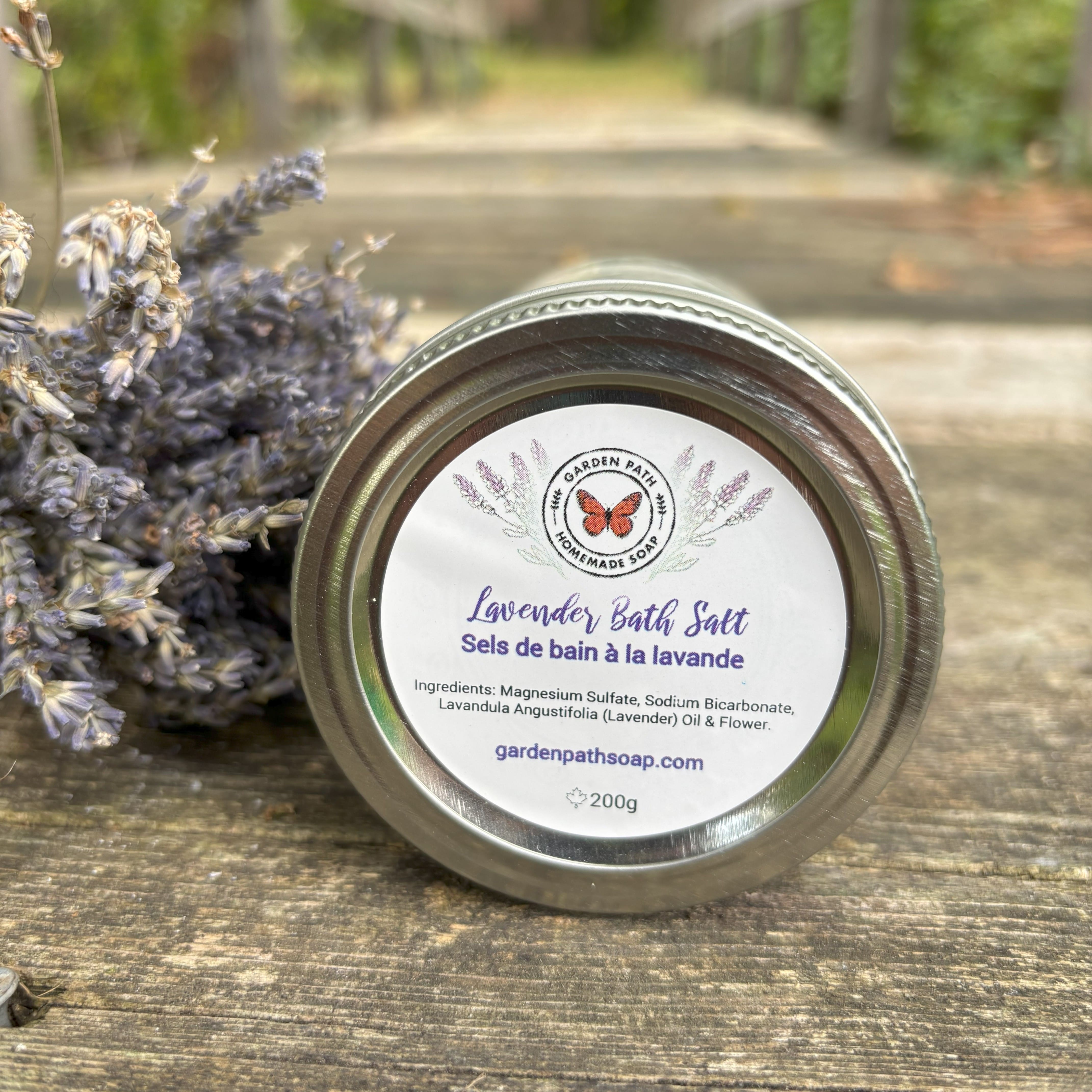 Jar of lavender bath salt with a label on a wooden surface with lavender flowers by Garden Path Homemade Soap. 100% Natural Essential Oil & Ingredients.