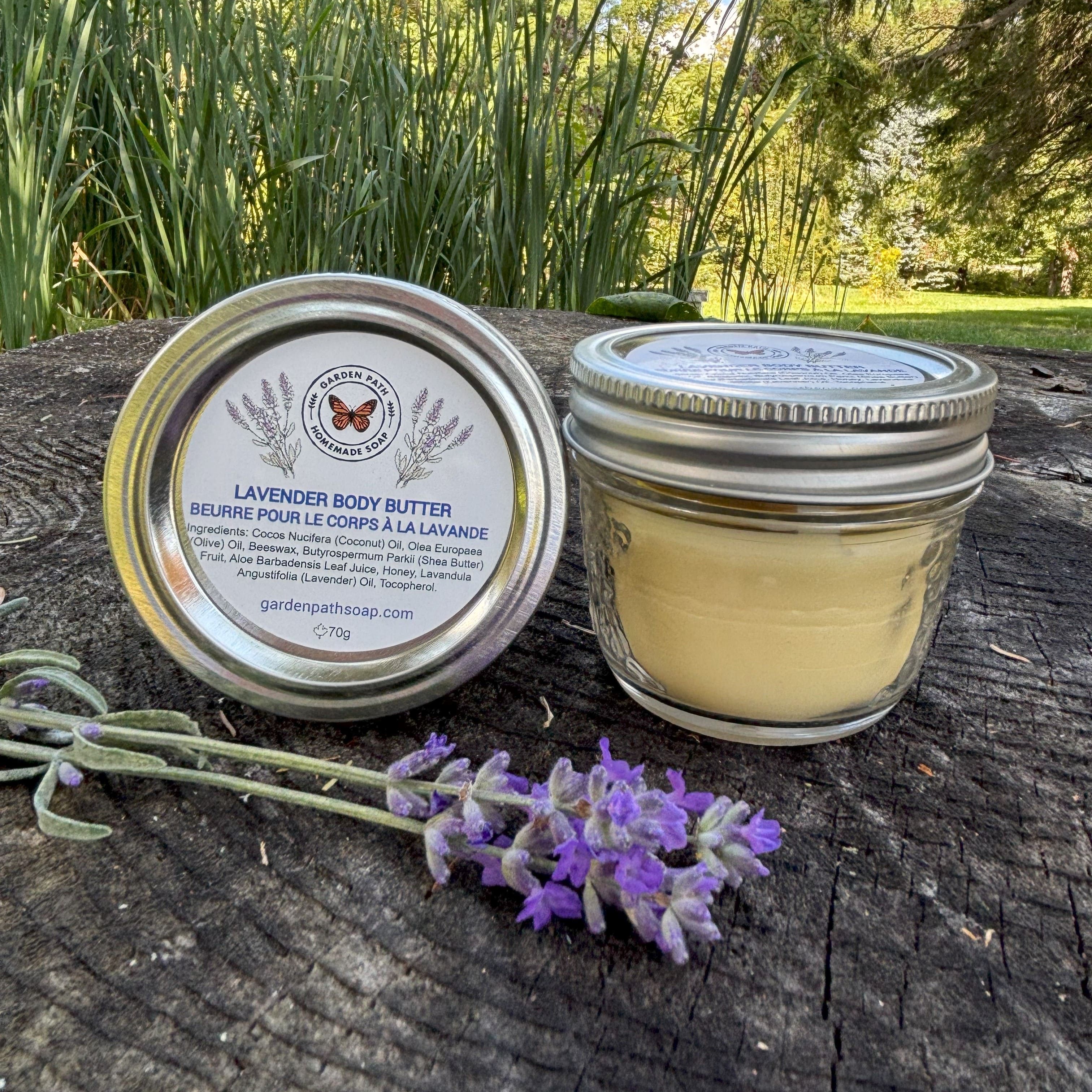 Jar of Lavender Body Butter with lavender flowers on a stump in a outdoor garden setting by  Garden Path Homemade Soap. 100% Natural Essential Oil- Intense Moisturizer