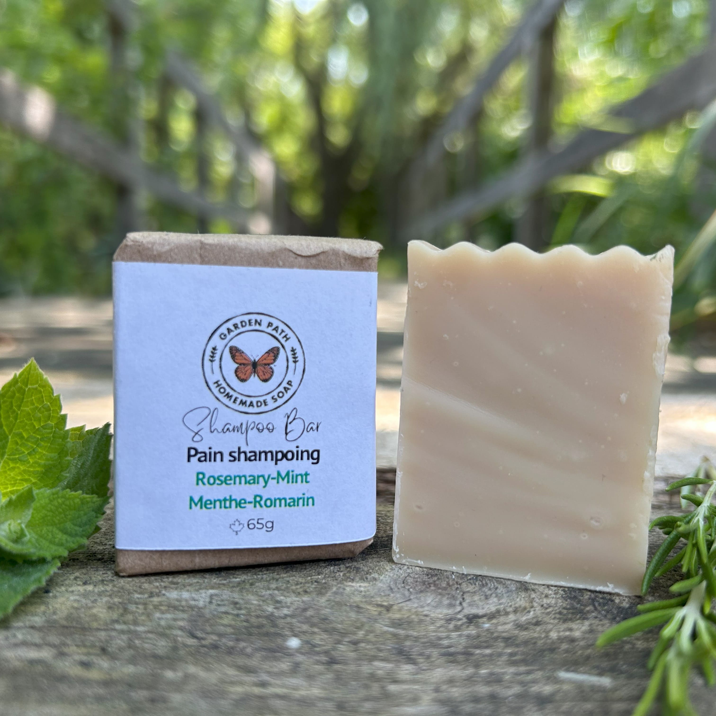 Mini wrapped and unwrapped Rosemary Mint Shampoo Bar by Garden Path Homemade Soap on wooden surface with mint and rosemary springs. 100% Natural Ingredients | Made with Beer