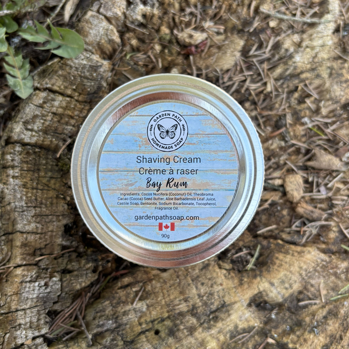 Shaving cream tin labeled "Bay Rum' on a wooden surface with natural background by Garden Path Homemade Soap.