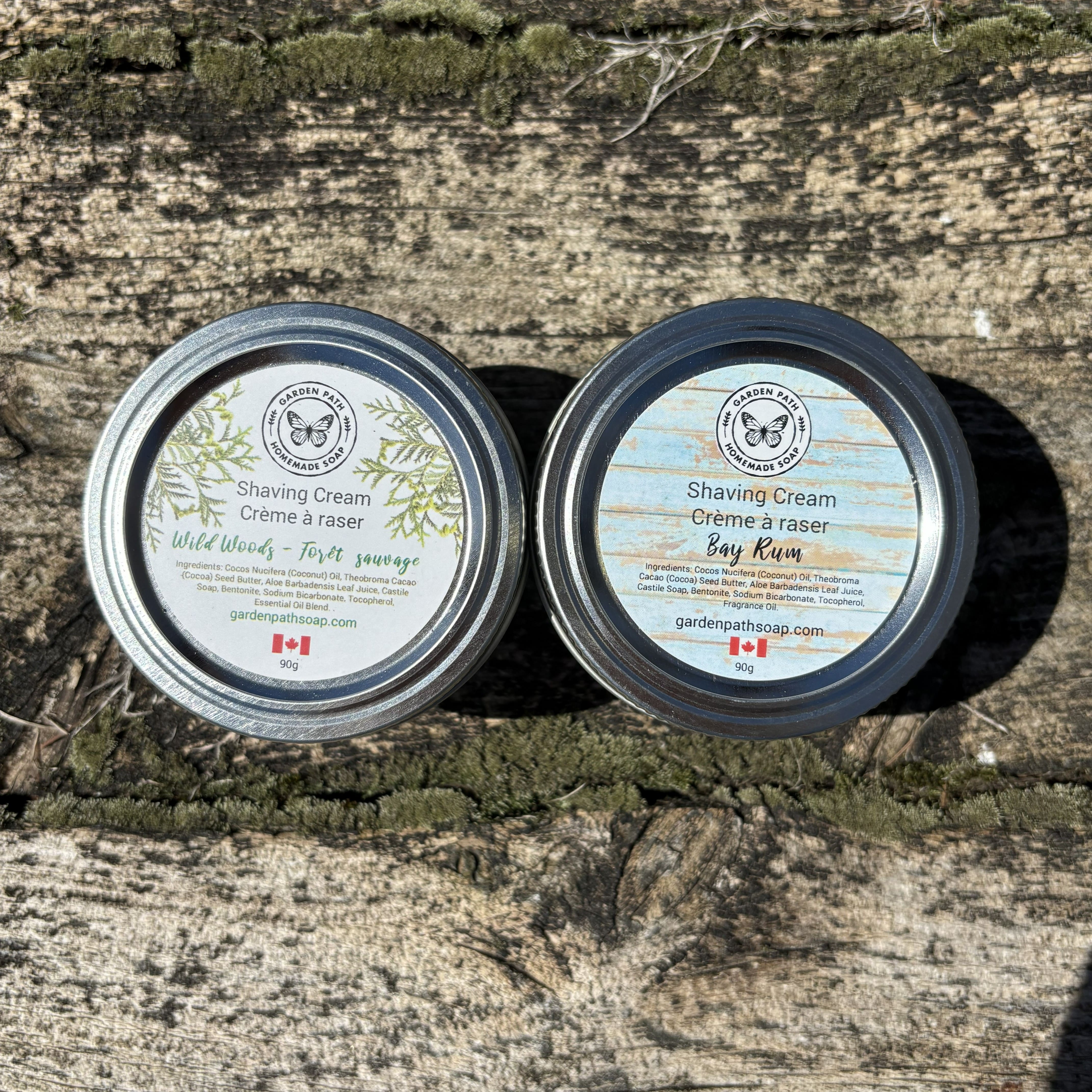 Two tins of shaving cream (Wild woods and Bay Rum) on a wooden surface by Garden Path Homemade Soap