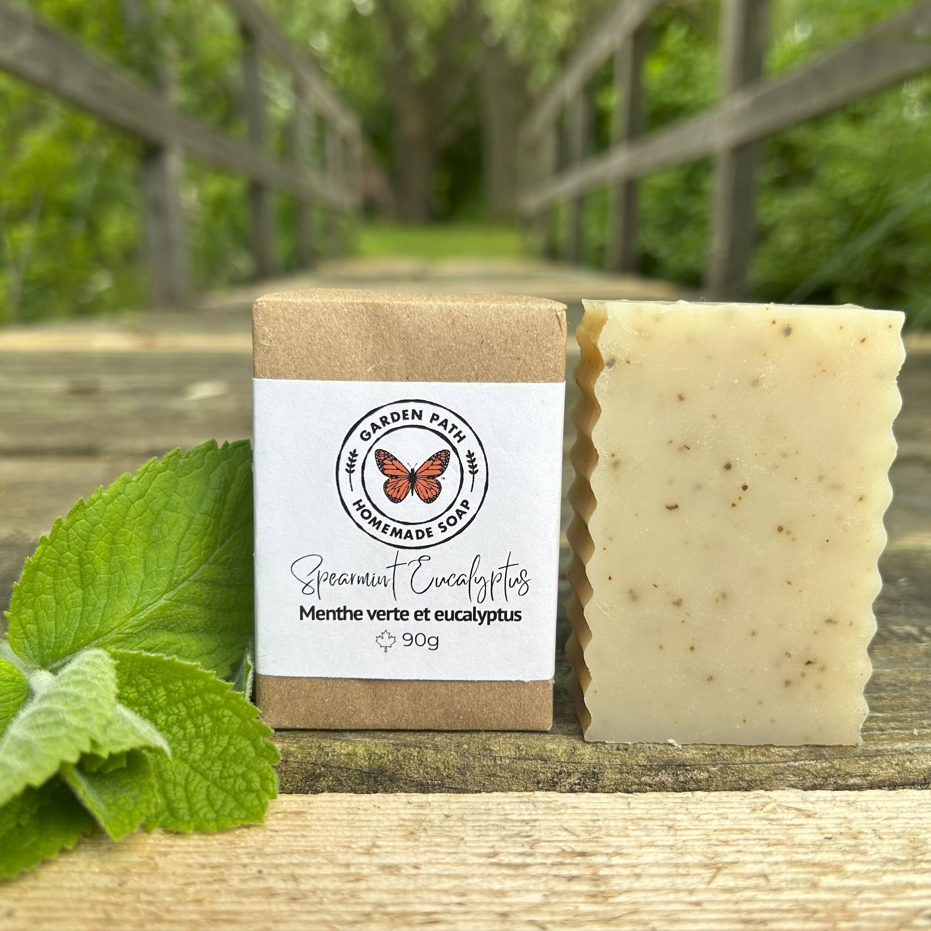 Spearmint Eucalyptus Bar Soap on a wooden surface with mint leaves beside the wrapped and unwrapped bars. | 100% Natural Essential Oils & Ingredients - Garden Path Homemade Soap