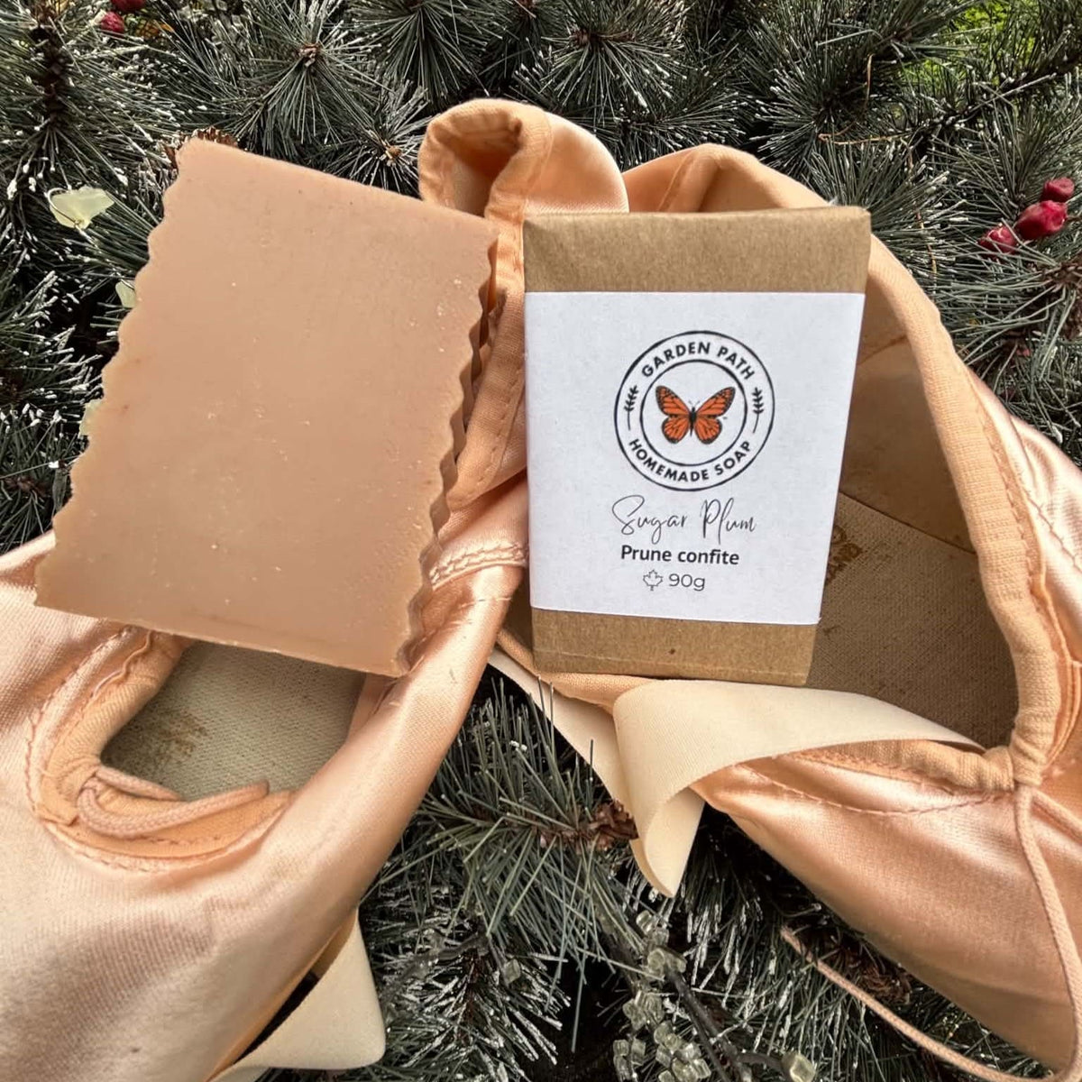 Tan coloured bar soap beside a wrapped bar of soap on a pair of ballet slippers with a green background. Garden Path Homemade Soap.