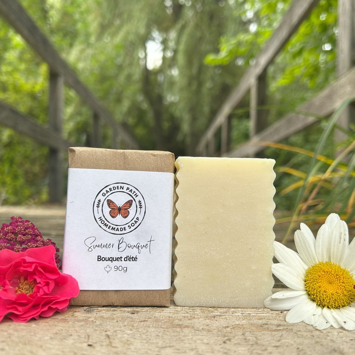 Summer Bouquet Bar of soap with a label, surrounded by flowers and a wooden background.  Garden Path Homemade Soap. Lightly scented with fragrance 