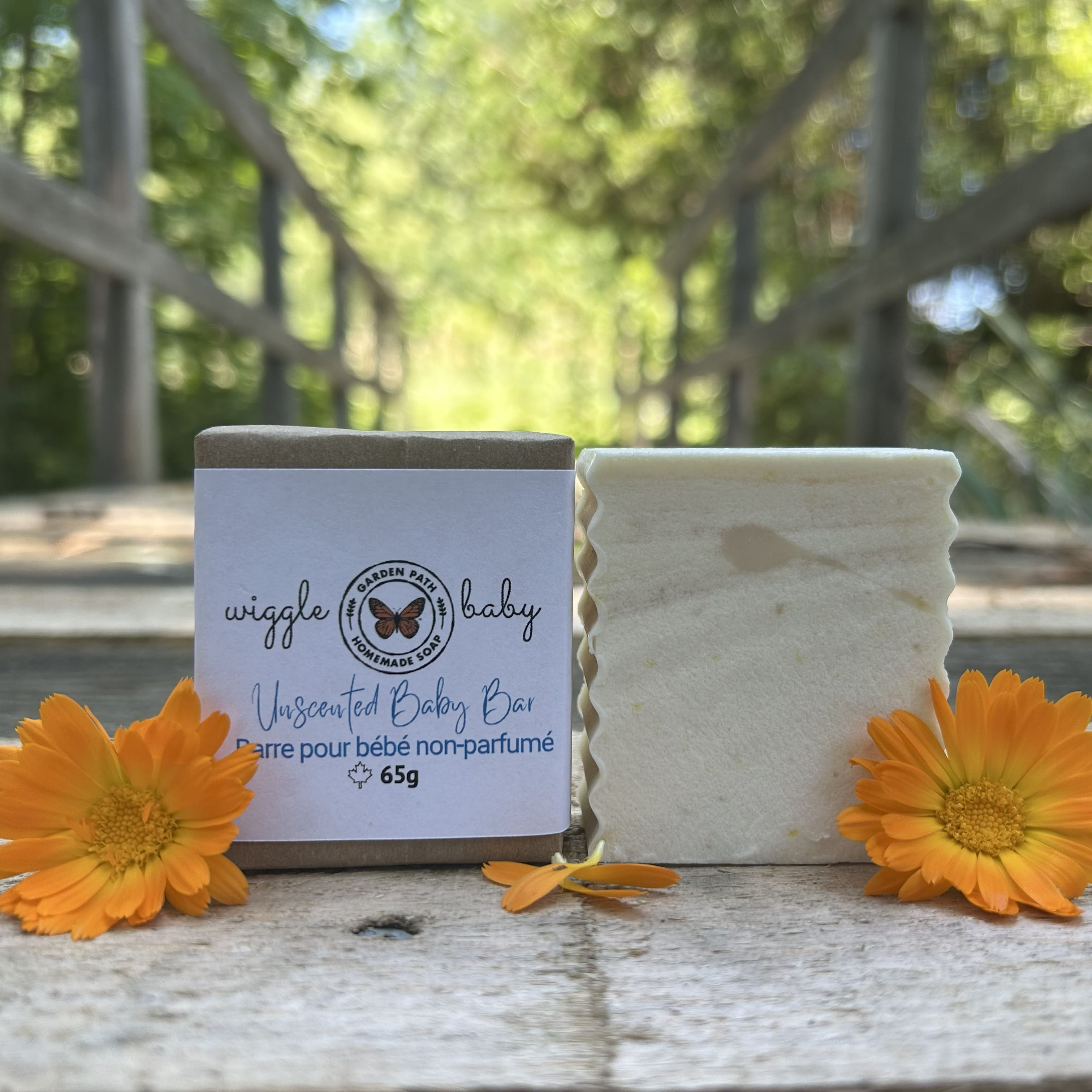 Wiggle Baby Bar both wrapped and unwrapped by Garden Path Homemade Soap sitting on a wooden  surface with calendula flowers. 100% Natural Ingredients | Unscented