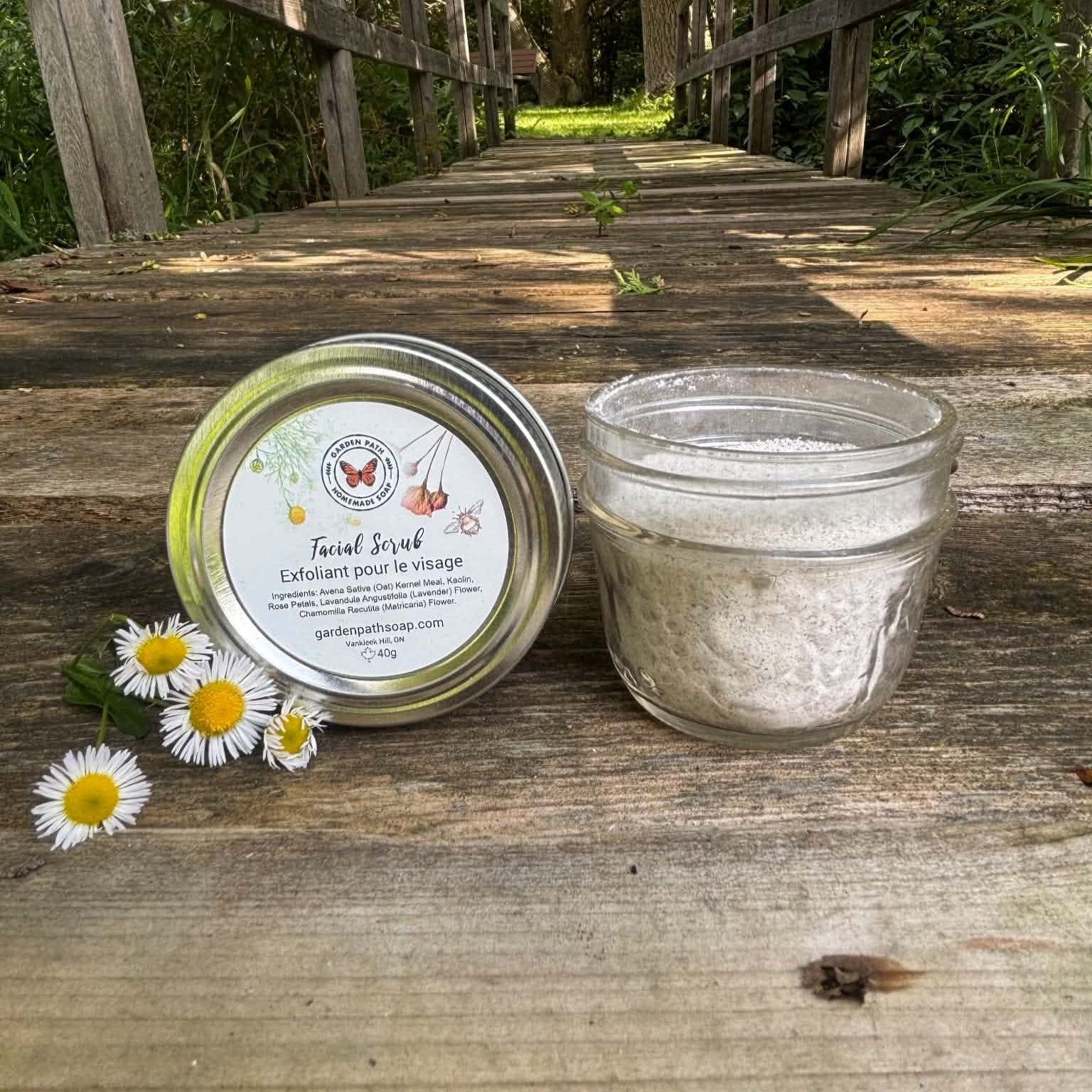 Jar of face scrub with a metal lid on a wooden surface with a natural background by Garden Path Homemade Soap. 100% Natural Ingredients