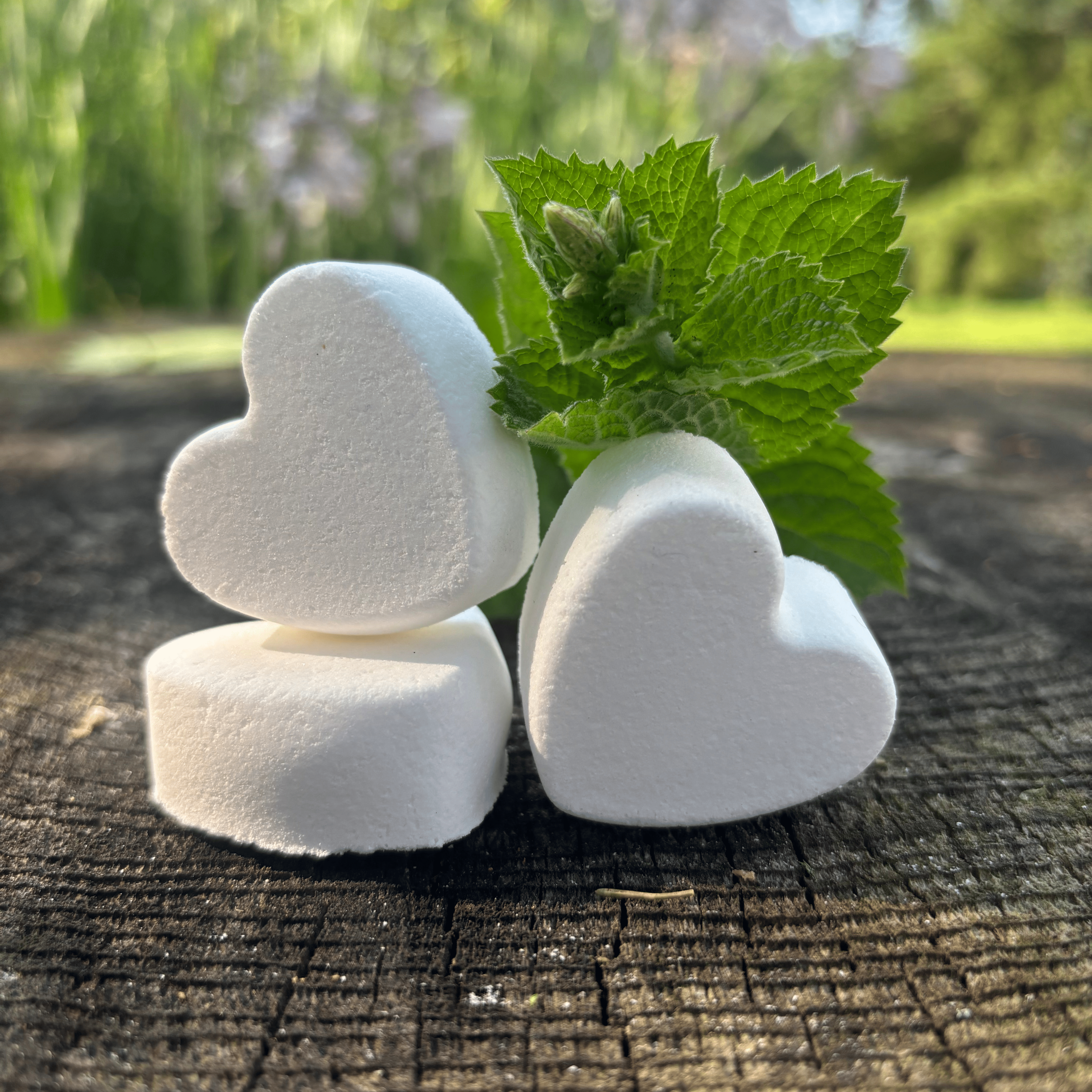 3 heart shaped Foot Fizzes on a wooden surface with peppermint springs by Garden Path Homemade Soap. 100% natural ingredients