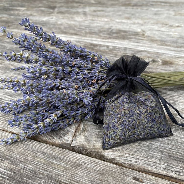 Lavender buds in an organza bag with a few sprigs of lavender on a wooden surface