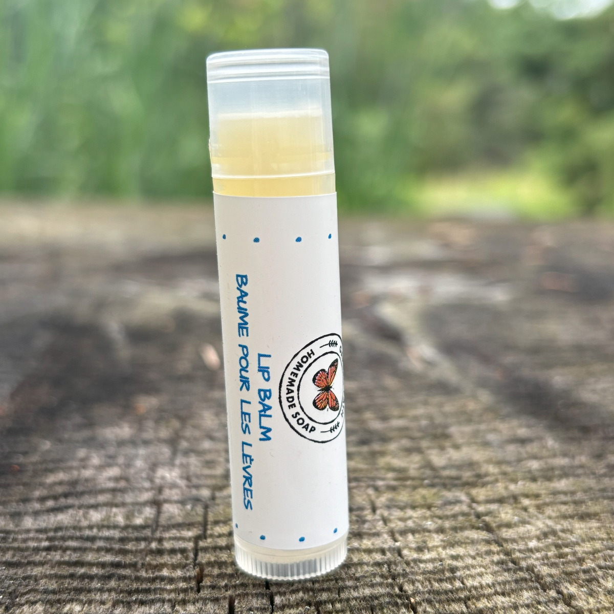 A tube of  100% natural ingredient lip balm placed on a wooden surface with a green background by Garden Path Homemade Soap