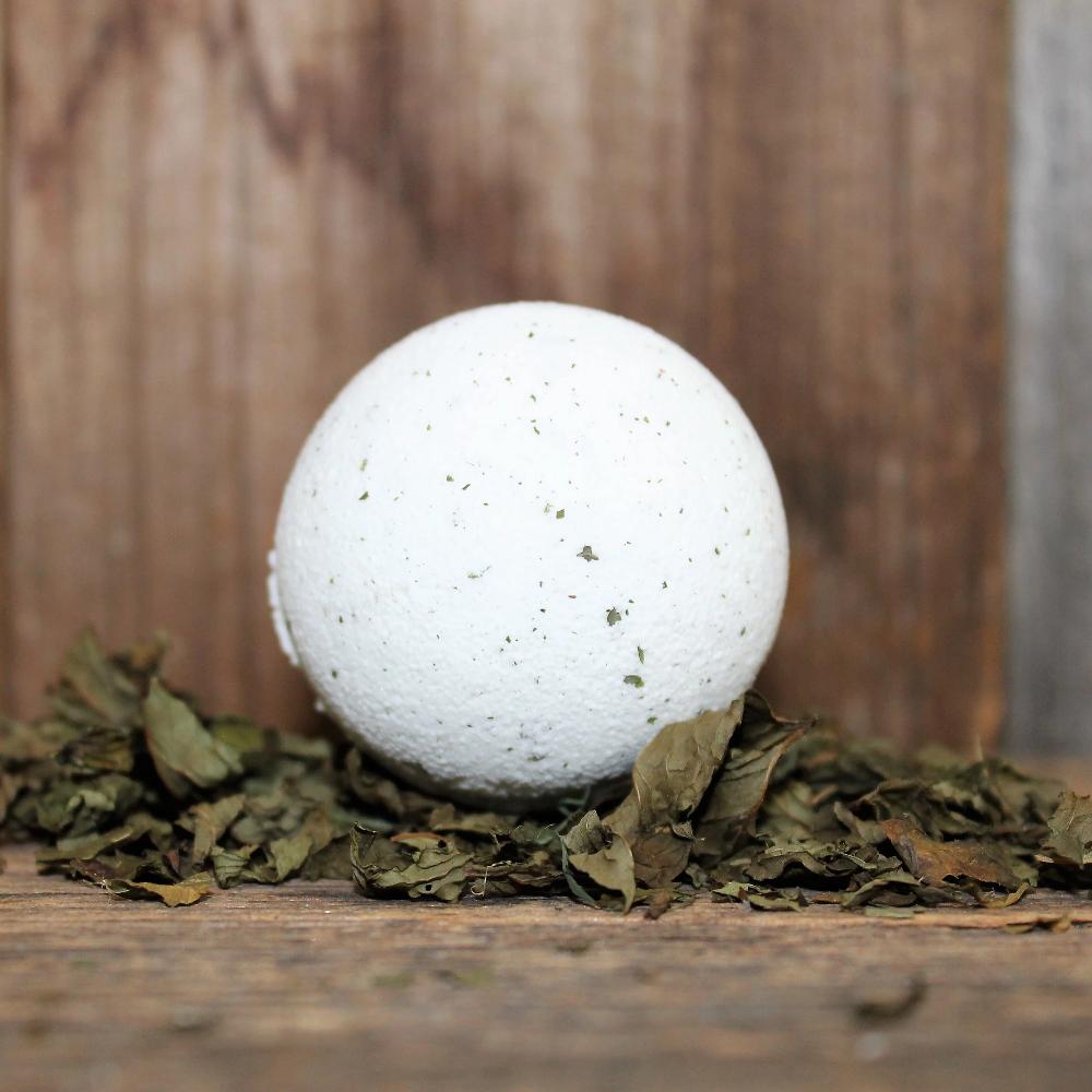 Breathe Bath Bomb sitting on top of green herbs on a wooden surface 