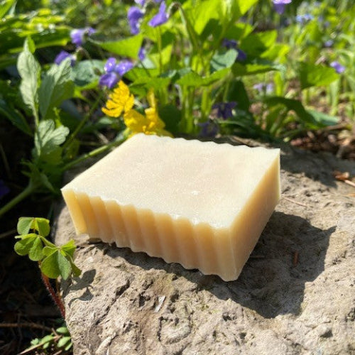 Unwrapped summer bouquet bar of soap on a large rock with flowers in the background. Lightly Scented with Fragrance. Garden Path Homemade Soap