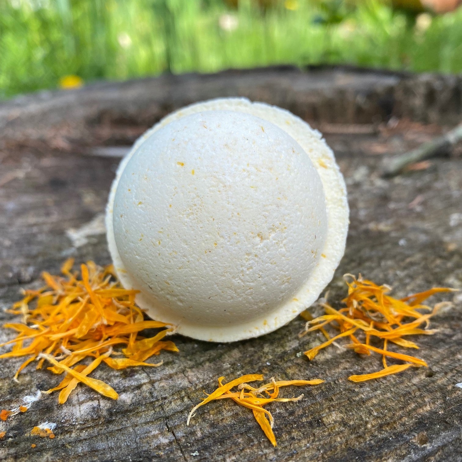 Sunny Delight Bath Bomb sitting on a wooden surface with yellow petals scattered around by Garden Path Homemade Soap