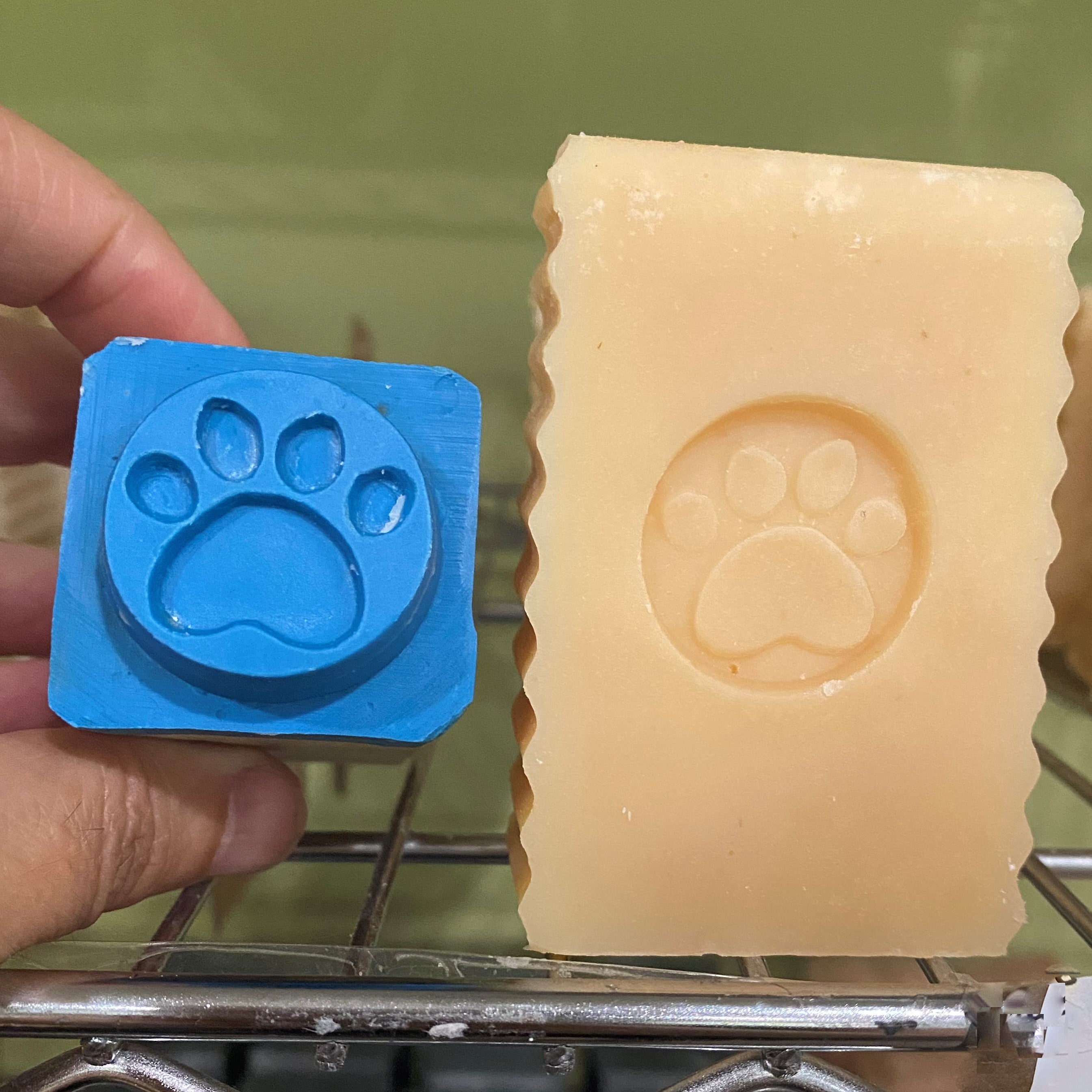 Unwrapped dog bar soap with an imprint of a dog's paw on the soap and the dog paw stamp beside the soap by Garden Path Homemade Soap. 