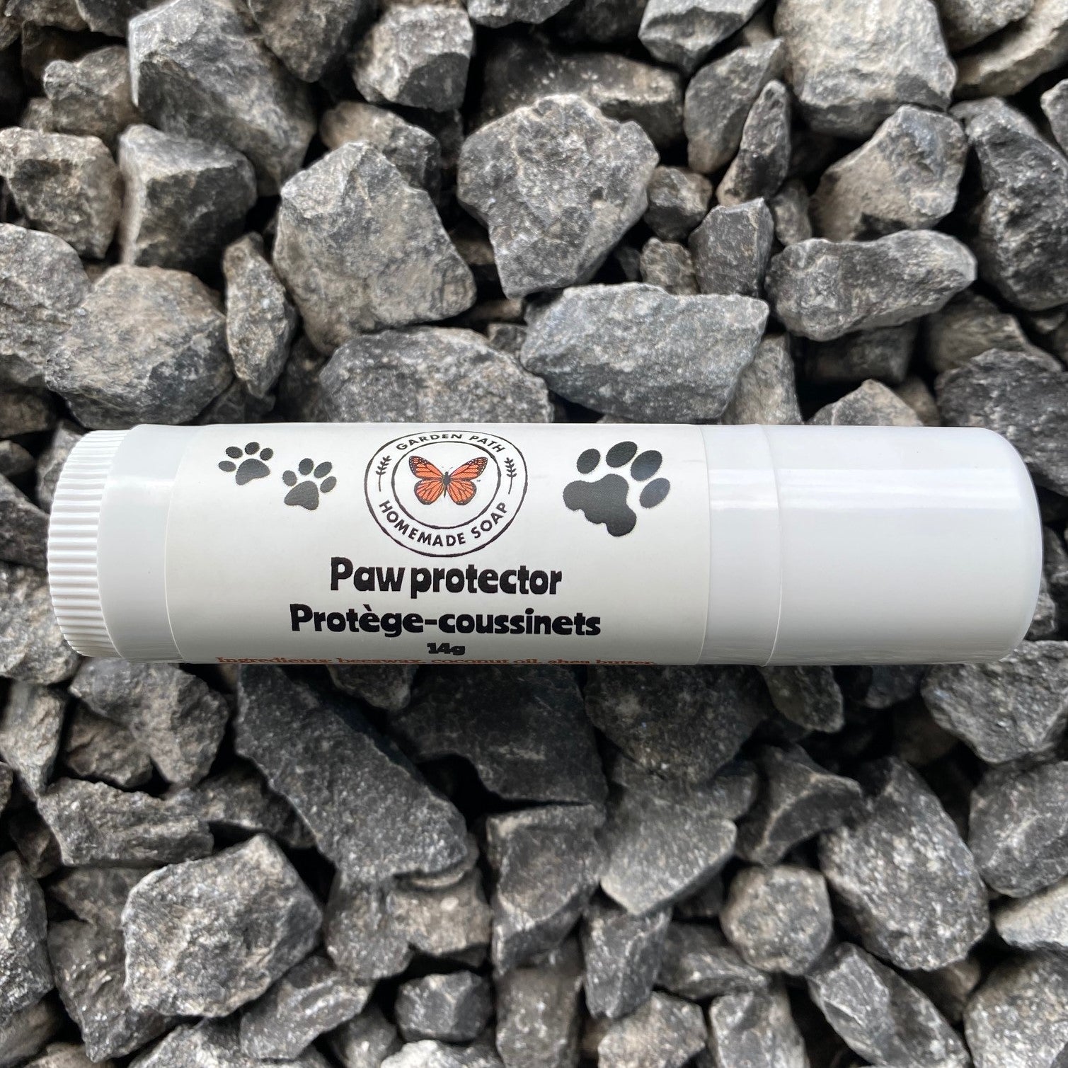 A roll-up tube of paw protector cream placed on a bed of rocks, with the product's branding and text visible on the tube.