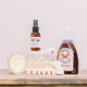 A variety of products like body spray, foaming hand wash, green tea face cream, wooden pine soap dish, opened jar of body butter, bath bomb and shower tablets